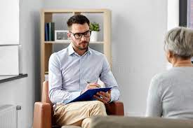 woman with gray hair sits across from male therapist holding clipboard